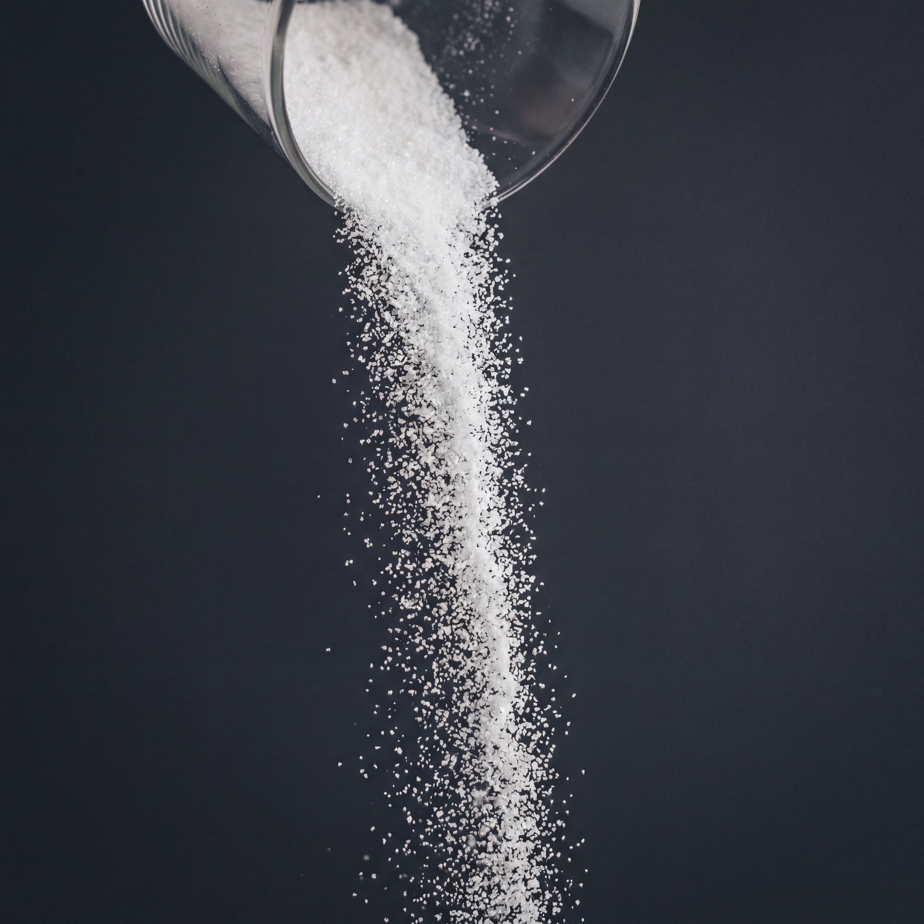 Fine powder pouring through dark studio light, representing a fragile raw active before delivery