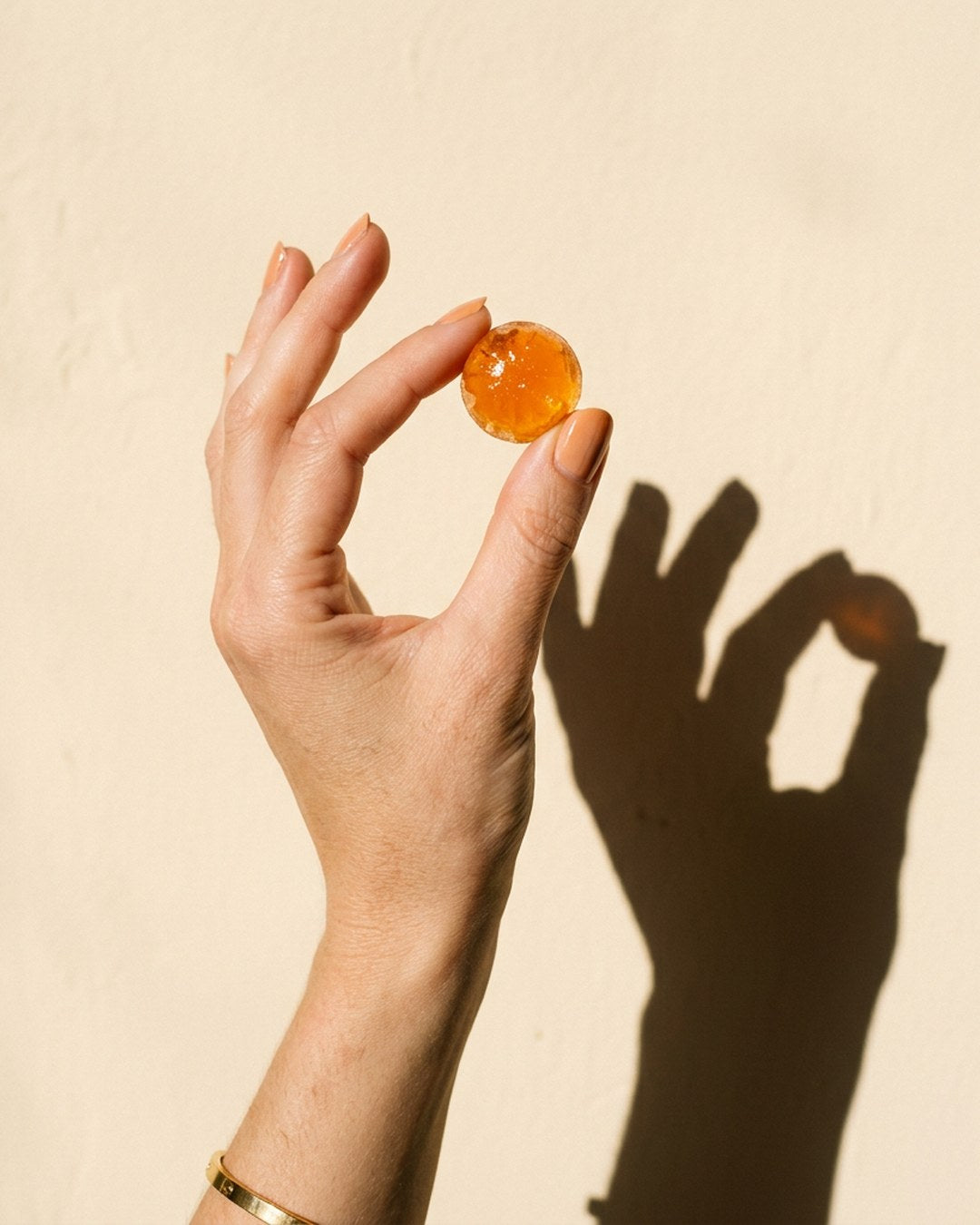 A TW-02 citrus gummy held up like a gem against a sunlit cream wall